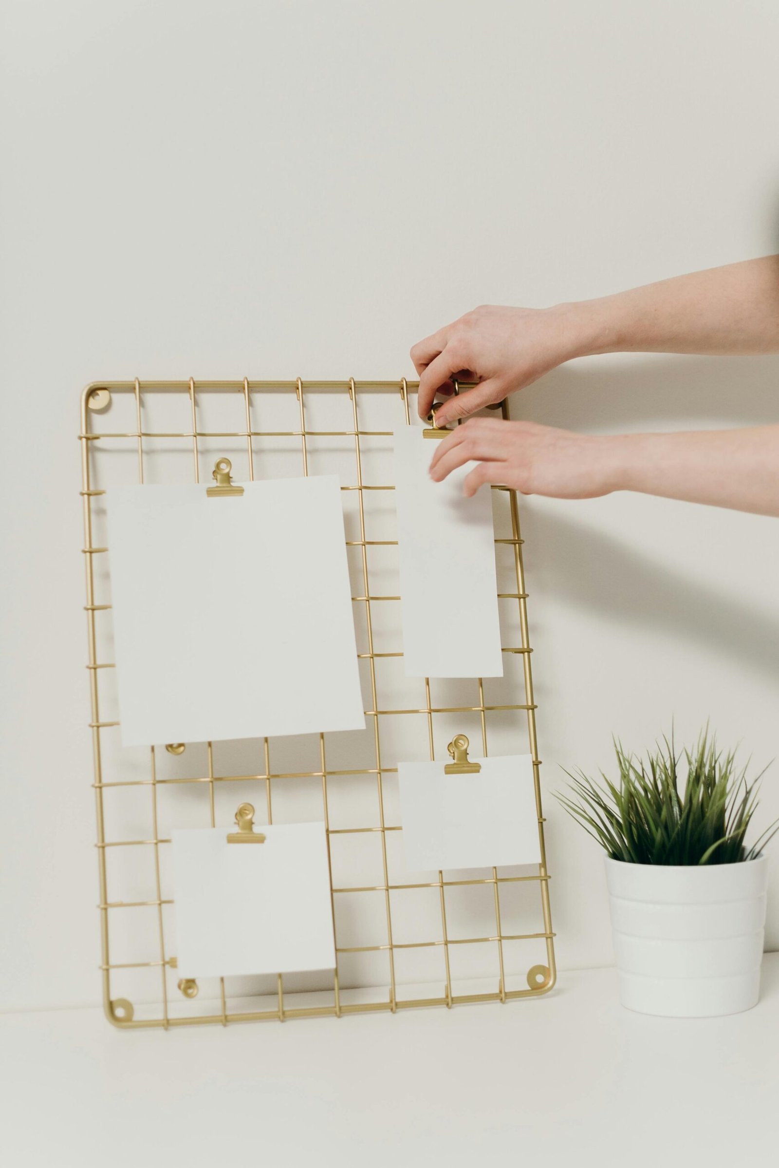 A minimalist arrangement with a golden mesh clipboard displaying blank notes, alongside a potted plant.