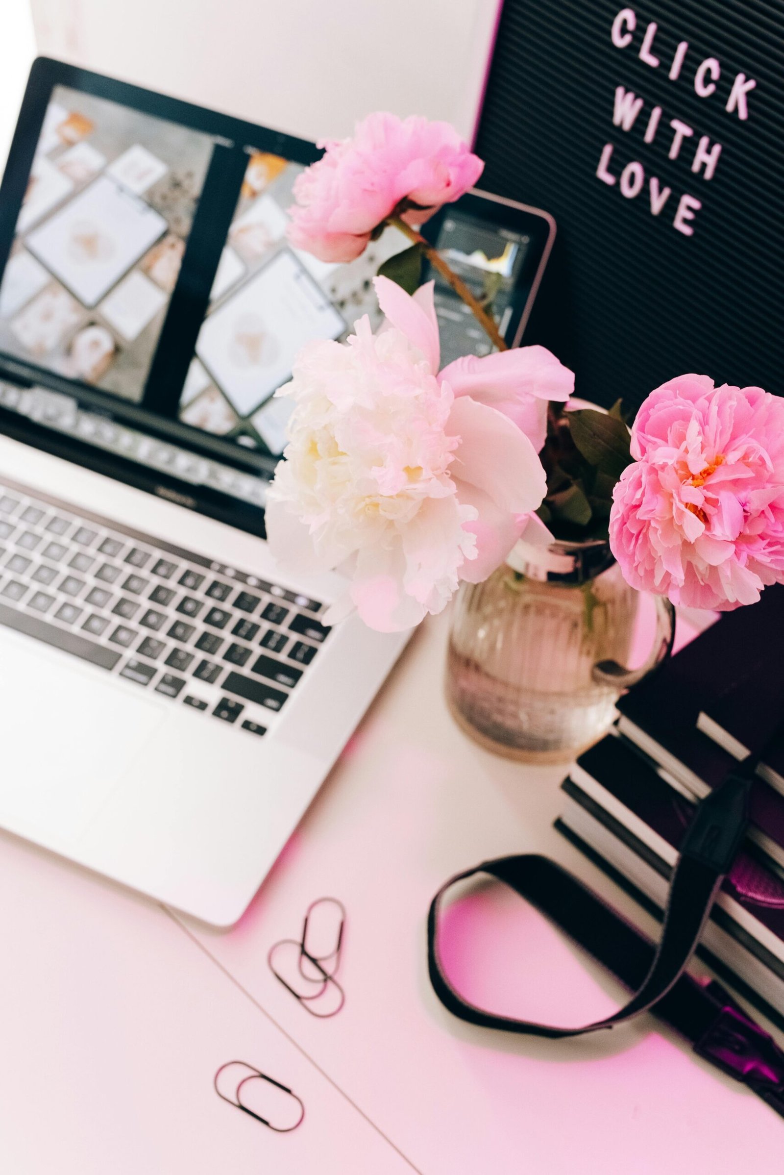 Aesthetic workspace with a laptop, pink peonies, and a letter board reading 'Click with Love'.